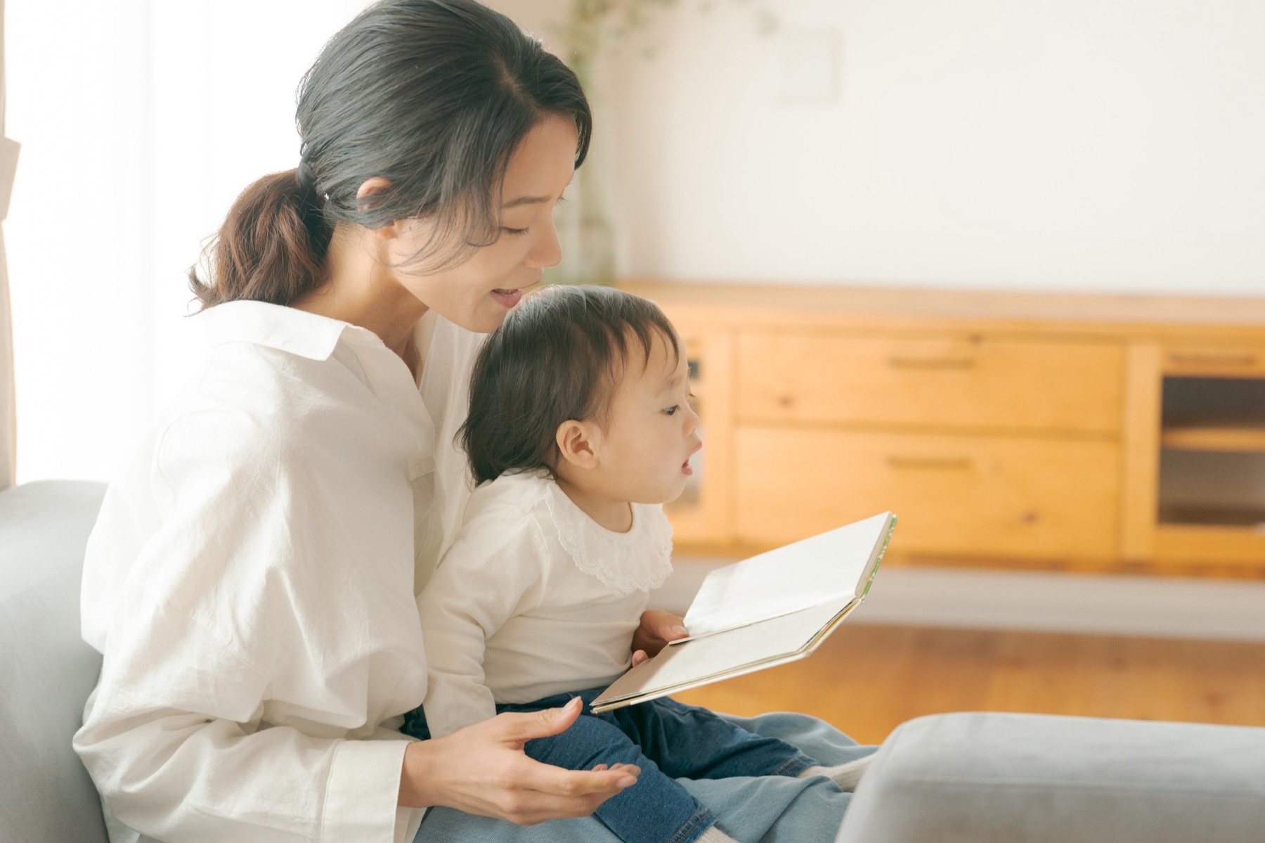 ソファで、赤ちゃんに絵本を読み聞かせるお母さん